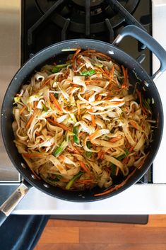 a wok filled with noodles and vegetables on top of a stove burner next to an oven