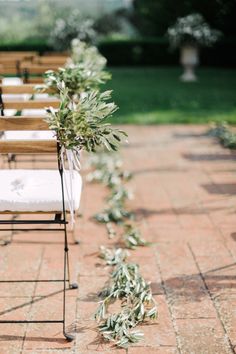 an outdoor ceremony with chairs and greenery on the aisle, ready for guests to sit down