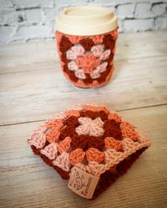 two crocheted coasters sitting on top of a wooden table next to a coffee cup