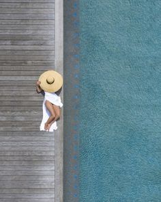 a woman with a hat on her head leaning against a wall next to the water