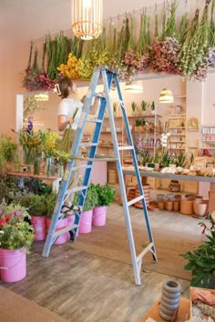 a woman is climbing up a ladder in a flower shop