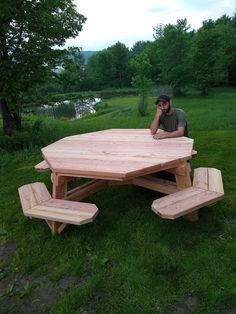 a man sitting at a picnic table in the middle of a field with benches around it