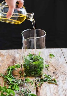 someone is pouring water into a glass filled with green herbs on a wooden table top