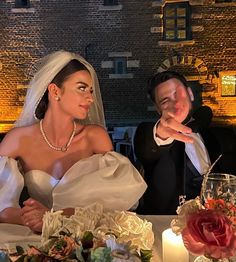 a man and woman sitting at a table with candles in front of them, one wearing a wedding dress