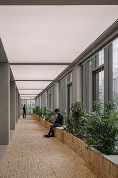 a man sitting on a bench in an empty building next to tall windows and plants