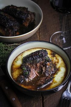 a bowl of food with some meat in it and a glass of wine next to it