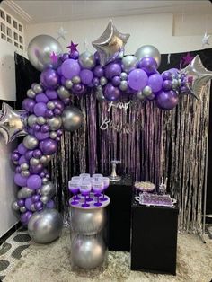 a purple and silver balloon arch with streamers on the top, balloons in the middle