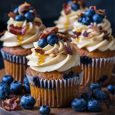 cupcakes with frosting and blueberries on a wooden board next to some bacon