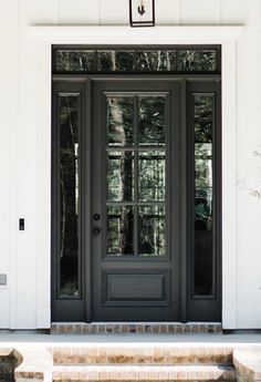 a black front door with two sidelights and brick steps