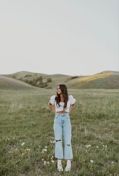 a woman standing in the middle of a field with her hands on her hips and looking up