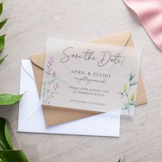 an envelope with some flowers on it next to a pink and white ribbon that says save the date