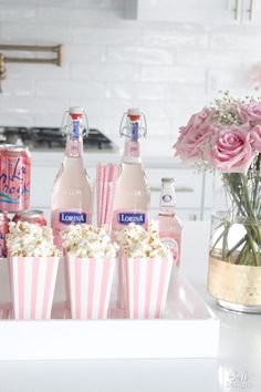 pink and white striped paper cups filled with popcorn next to bottles of soda, water and flowers