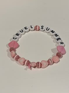 a pink and white bracelet with seashells on it that says cruel summer written in small letters