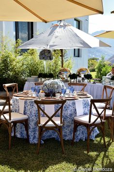 an outdoor table set up with blue and white linens, umbrellas and chairs