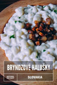 a wooden plate topped with mashed potatoes covered in white sauce and garnished with chopped nuts