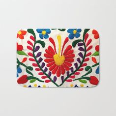 an embroidered bath mat with colorful flowers and leaves on white background, including red, blue, green, yellow, orange, and purple colors