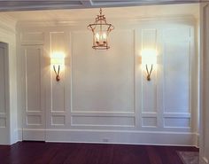 an empty room with two lamps on the wall and hard wood floors in front of it