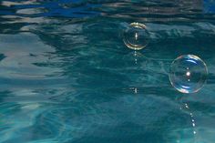 two bubbles floating on top of the water in front of a blue pool with ripples