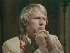 a man with blonde hair wearing a tan suit and red tie looking at the camera