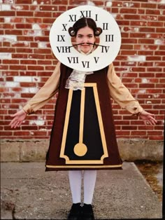 a woman wearing a clock costume standing in front of a brick wall with roman numerals on it