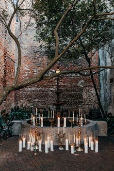 candles are arranged on a circular table in the middle of a brick courtyard with trees