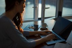 a woman sitting in front of a laptop computer on top of a wooden table next to a cup of coffee