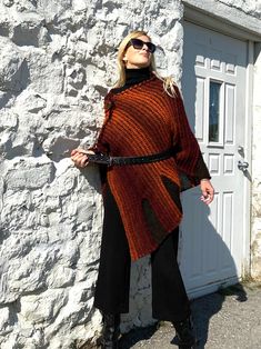 "Fall Knit Steampunk Ruffle Wrap | Boho Alpaca Black Orange Poncho, Wool Poncho Cape For Women This flirty, ruffled, alpaca wool blend hand-knitted wrap in black and burnt orange tons, is light and warm. It is a four-season piece and is ideal for layering.  The colour palette of this versatile shawl is definitely jeans friendly.  STYLE This dressy/casual piece is an excellent travel companion.  Works well with jeans, leggings, dress pants or over a solid dress adding a flowy elegance of a shawl. Endless in its versatility and fits most sizes make it a great gift idea. Material: Alpacas Wool Blend WAYS TO WEAR SEE FAQ's FOR WAYS TO WEAR AS A SHAWL, FITTED LOOK, BELTED LOOK AND SCARF. SIZING Length is approx. 30\" Fits sizes S- 3xl Please inquire about larger sizes Our model Elana is size 8 Knit Fabrication Poncho For Fall, One Size, Knit Fabrication One-size Poncho For Fall, One Size Knit Poncho For Fall, Acrylic Poncho Shawl For Fall, Acrylic Shawl Poncho For Fall, Fall Festival Cape Poncho, One Size Acrylic Poncho For Fall, Bohemian Black Poncho For Fall, Knitted Shawl Cape For Fall