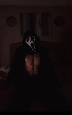 a man wearing a mask sitting on top of a bed in a room with dark lighting