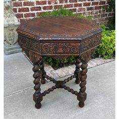 an old wooden table sitting on the sidewalk next to a brick wall and shrubbery