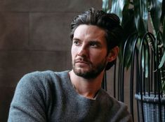 a man sitting in front of a potted plant looking at the camera with a serious look on his face