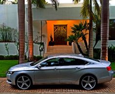 a silver car is parked in front of a house with palm trees and steps leading up to it