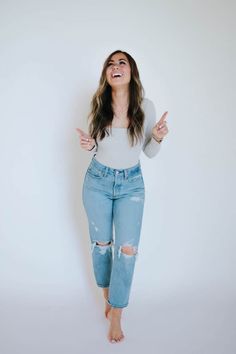 a woman standing in front of a white wall wearing ripped jeans and a tank top