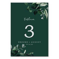 a table number card with leaves and greenery on it, in white text reads'3 brooke & august '