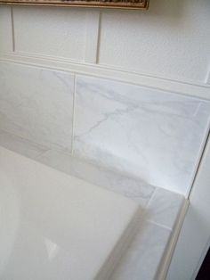 a bathroom with white marble tile and a gold framed picture on the wall above it