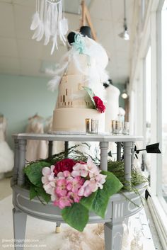 a wedding cake sitting on top of a table with flowers and feathers hanging from the ceiling