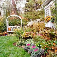 a garden with lots of plants and flowers in the grass next to a white arbor