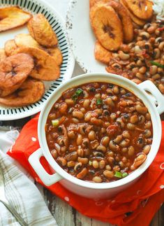 baked beans in a white bowl next to other plates of food on a wooden table