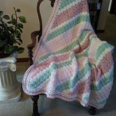 a crocheted blanket sitting on top of a chair next to a potted plant