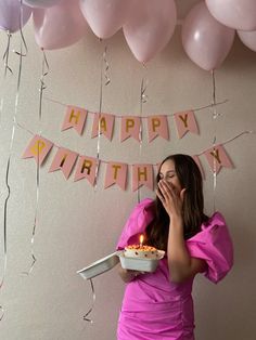 a woman holding a cake in front of her face with balloons and streamers around her