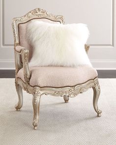 an antique chair with a white fur pillow on it's back and legs, in front of a wall