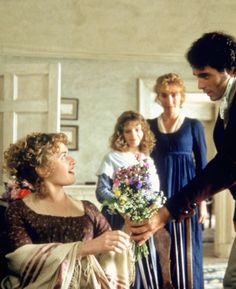 a man handing flowers to a woman in a room with two other people standing around