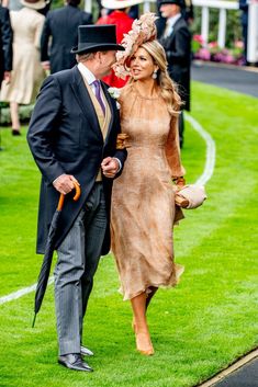 a man and woman dressed in formal attire walking down the grass at a horse race