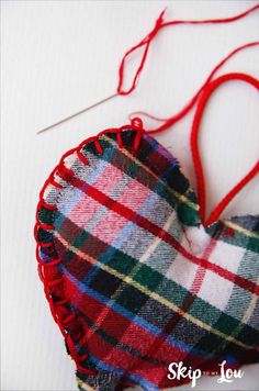 a heart shaped ornament with red thread on the end and plaid fabric hanging from it