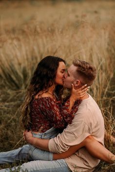 a man and woman sitting on the ground in front of tall grass kissing each other