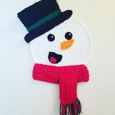 a crocheted snowman ornament hanging on a wall with a hat and scarf