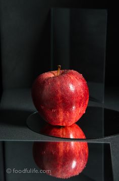 an apple sitting on top of a glass table next to a black wall and floor