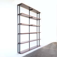 an empty book shelf in the corner of a room with white walls and concrete flooring