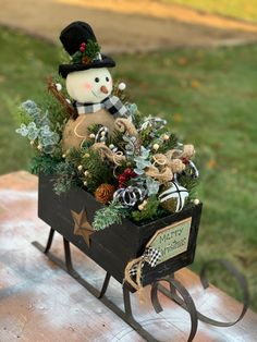 a snowman sitting on top of a wooden sleigh filled with christmas decorations