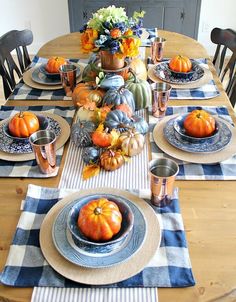 a dining room table set with blue and white placemats, pumpkins and flowers