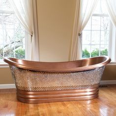 a bath tub sitting on top of a hard wood floor next to two large windows